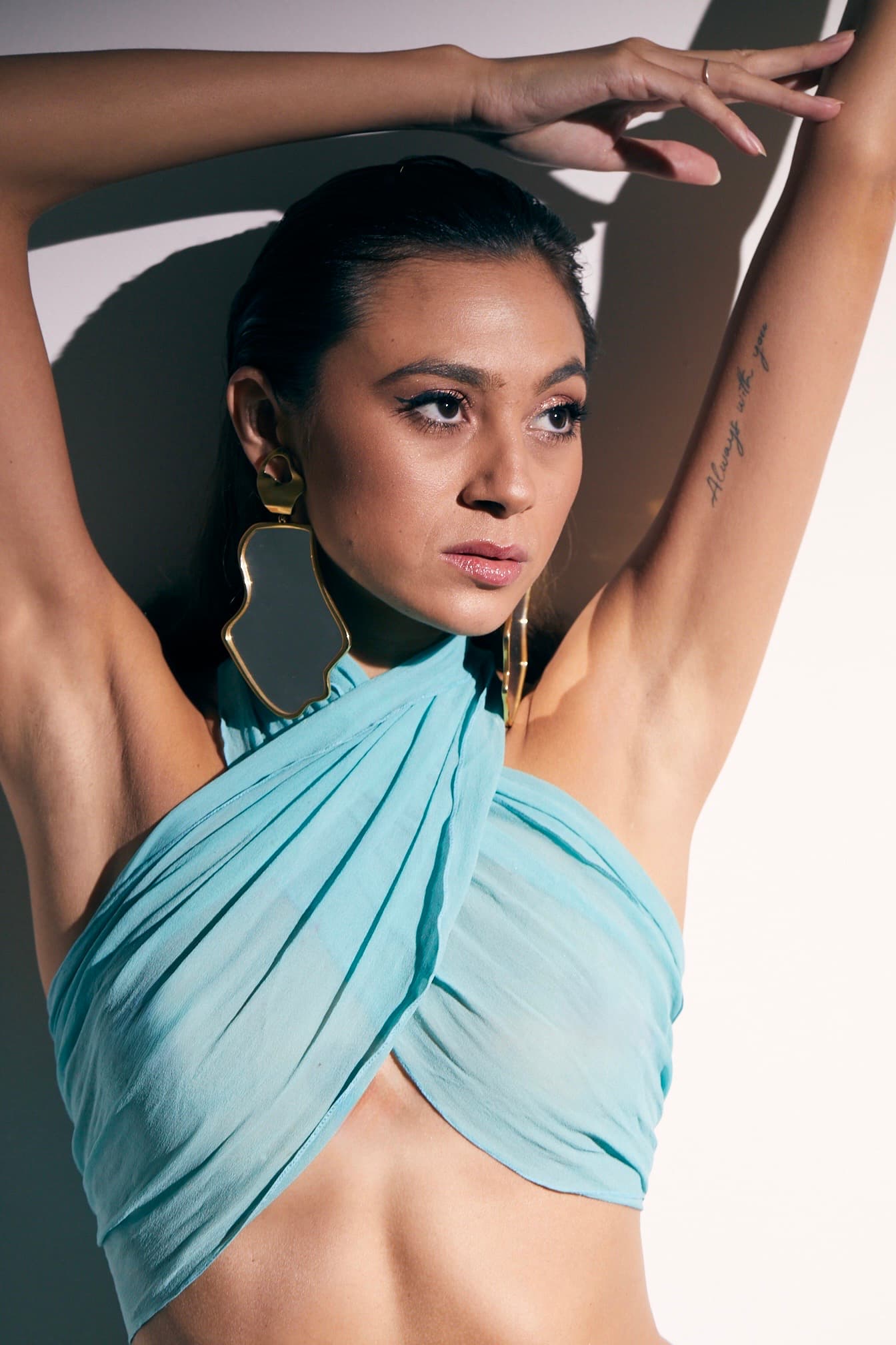 Julia Jones modeling an aqua fashion look and oversized sculptural earrings in direct beauty light
