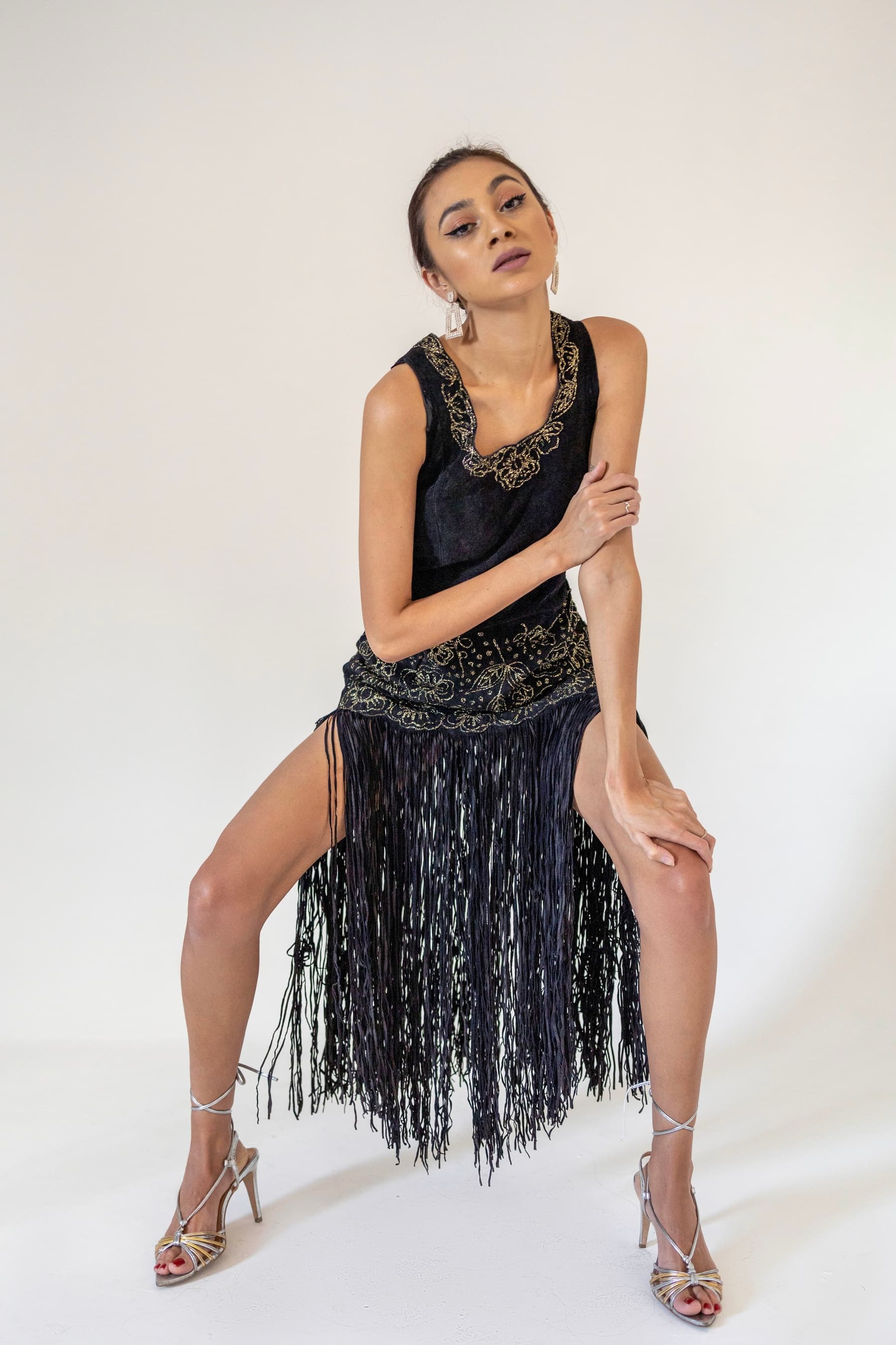 Julia Jones modeling a black-and-gold fringed dress and metallic heels in a studio