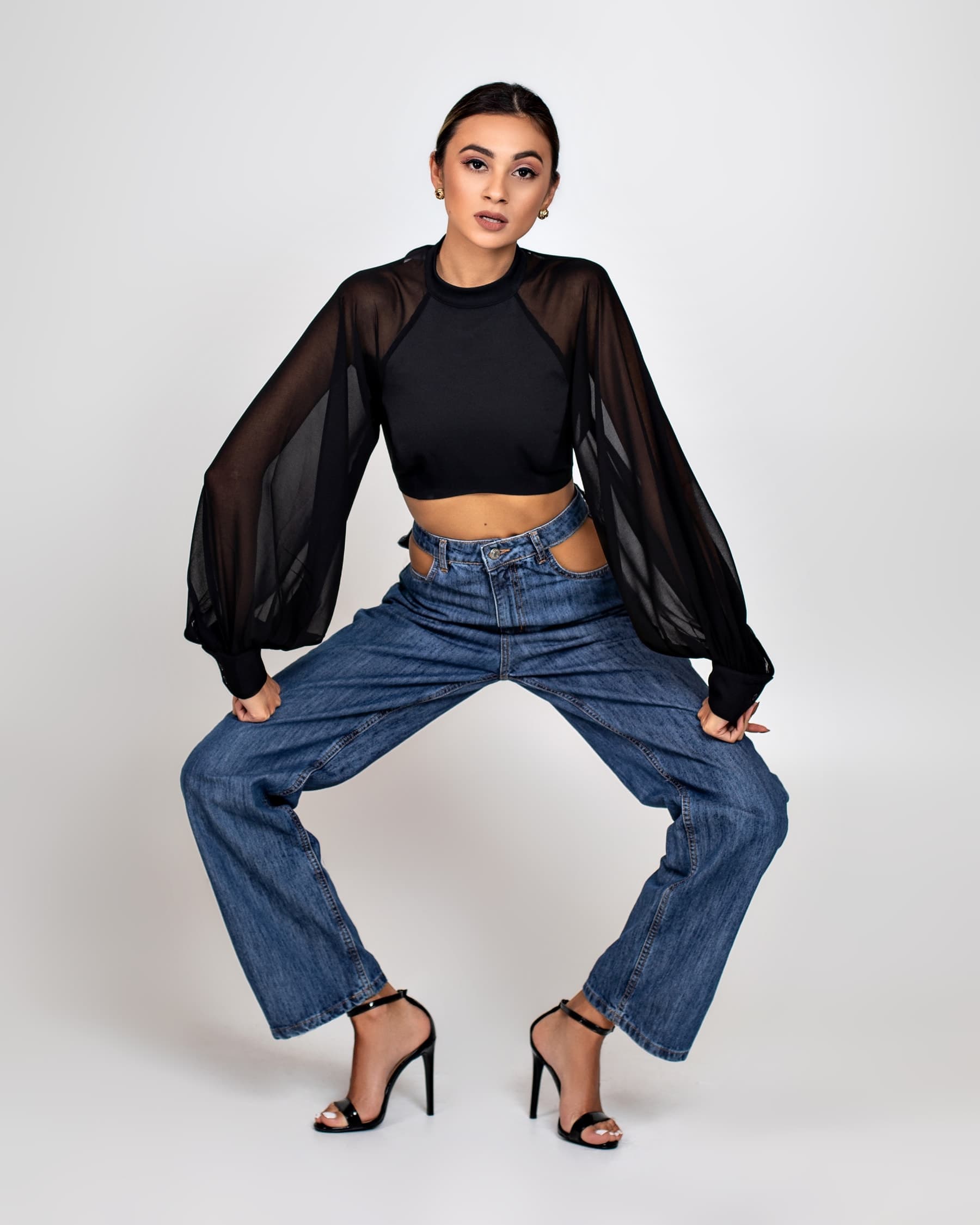 Julia Jones modeling wide-leg denim and a black sheer-sleeve top in a studio