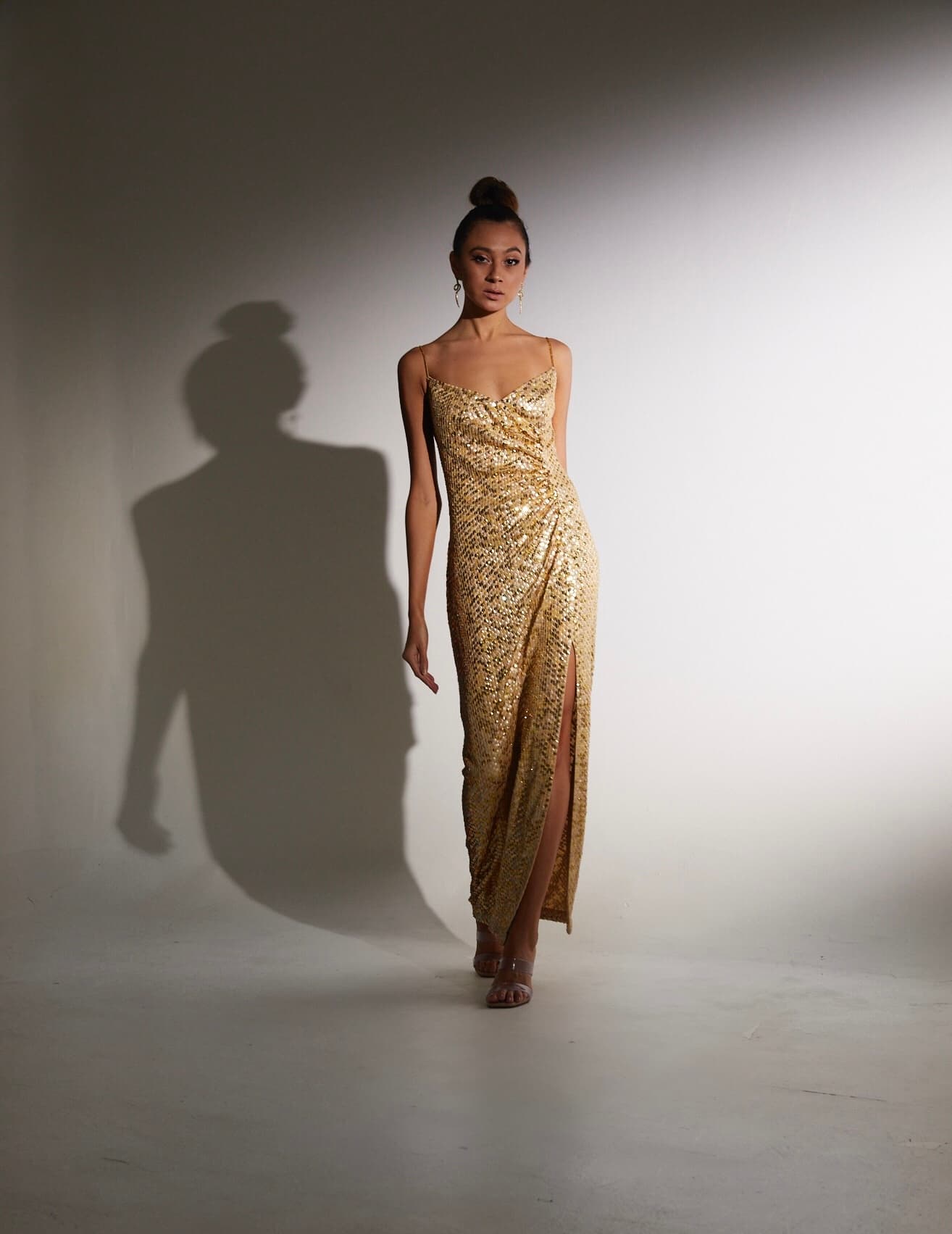 Julia Jones modeling a gold sequin gown in a full-length spotlight portrait