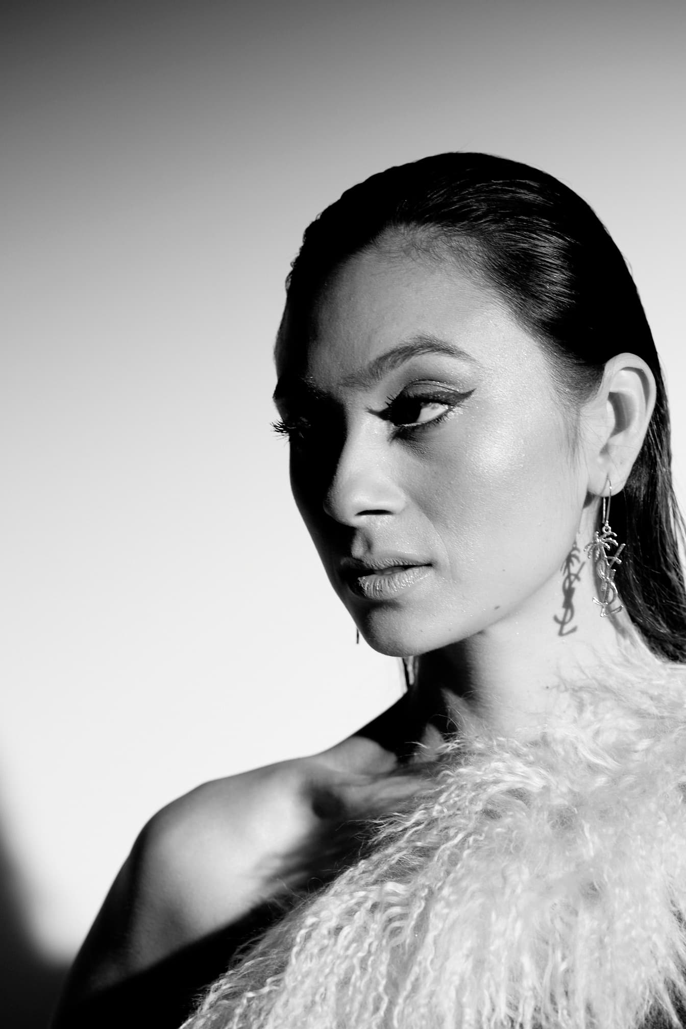 Black-and-white beauty portrait of Julia Jones wearing statement earrings and feather trim