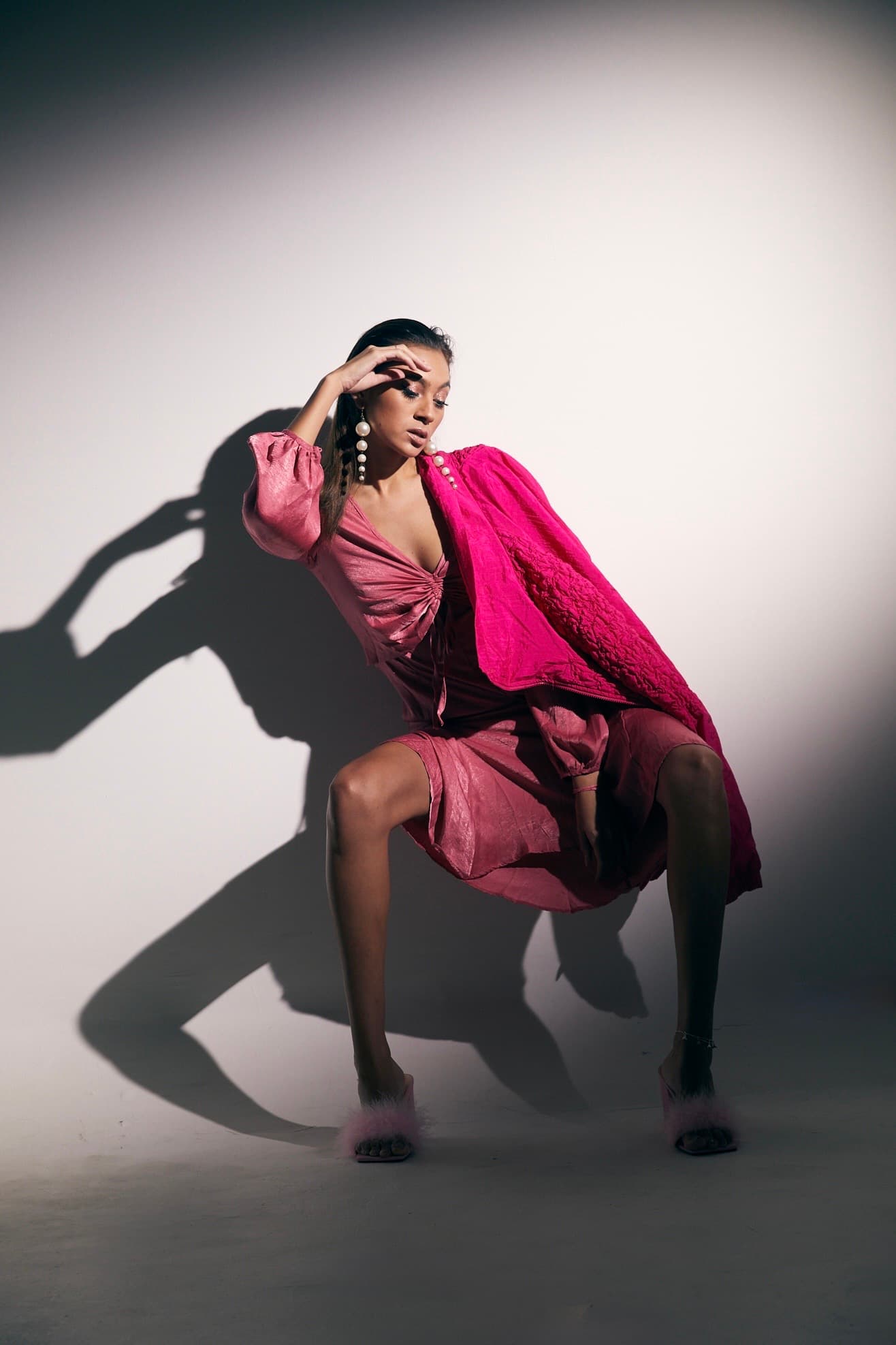Julia Jones modeling layered pink fashion and pearl earrings in a seated shadow portrait