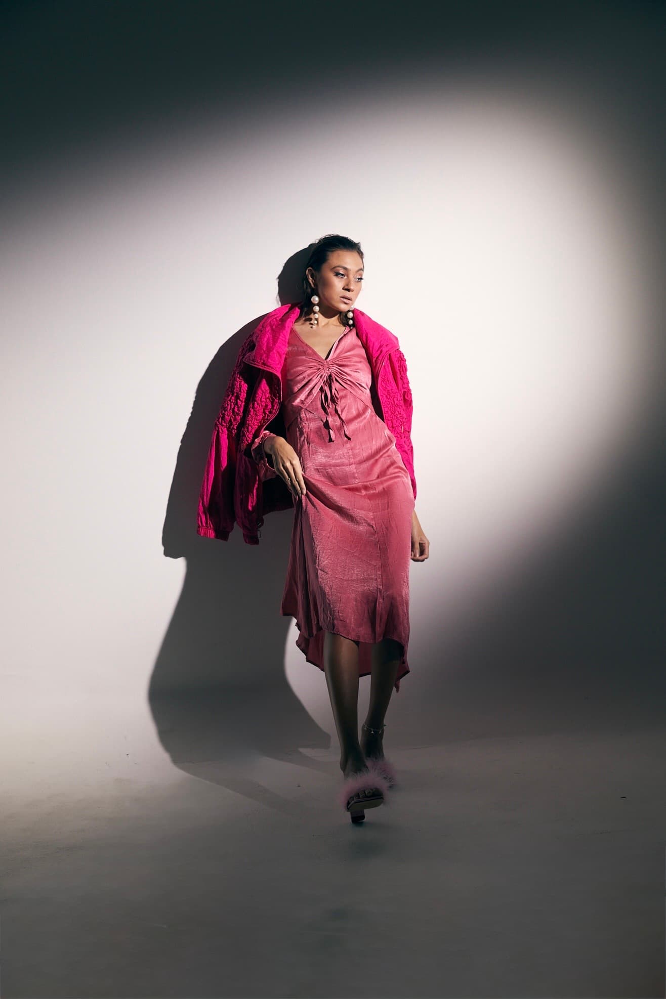 Julia Jones modeling layered pink fashion and pearl earrings in a full-body spotlight portrait